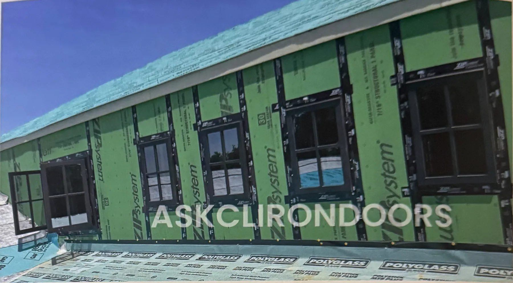 Row of dark-framed casement iron windows set into a house wrapped for new construction